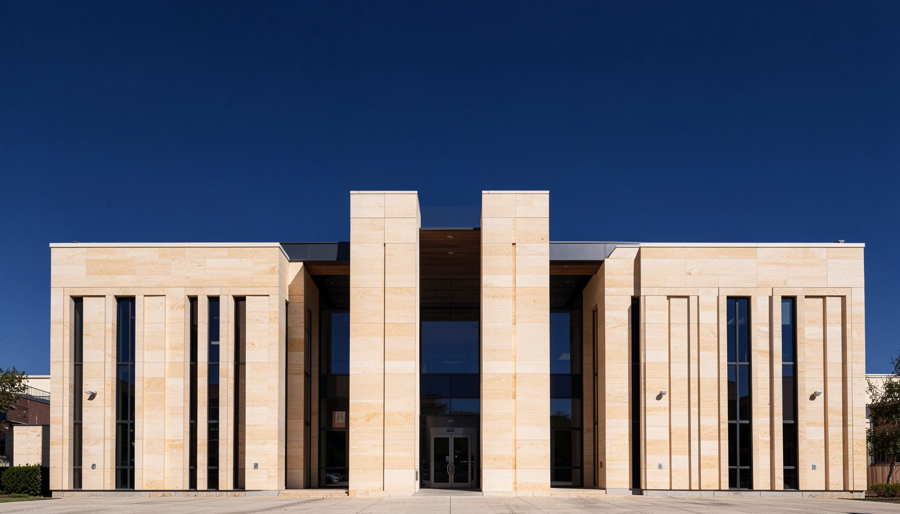 A clean architectural photograph of a modern civic building facade with strong symmetry, warm limestone tones, and deep blue sky